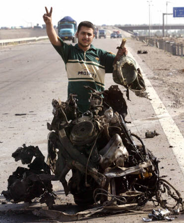 An Iraqi youth flashes a victory sign near the charred remains of one of two suicide car bombs, which were followed by clashes in Abu Ghraib, west of Baghdad, April 3, 2005. REUTERS/Ali Jasim 